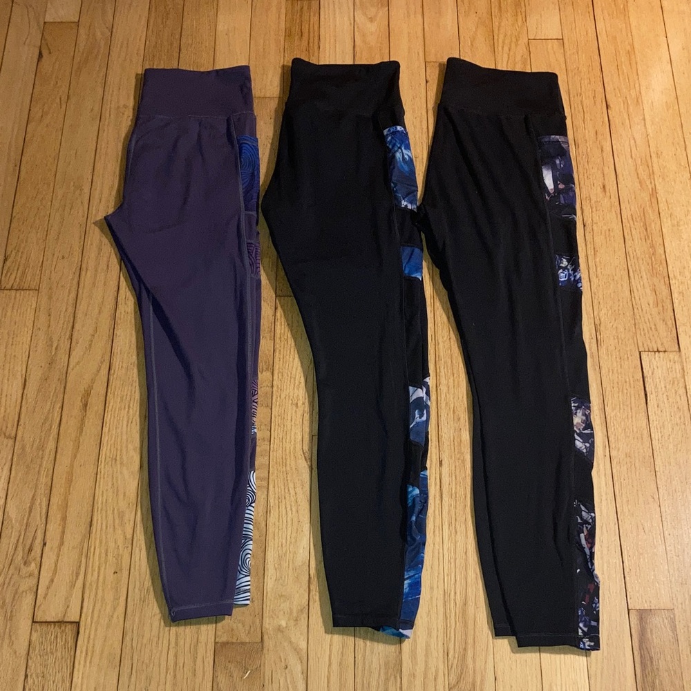 3 pairs of Leggings 1 Purple and 2 Black w/ color patterns on each leg side.